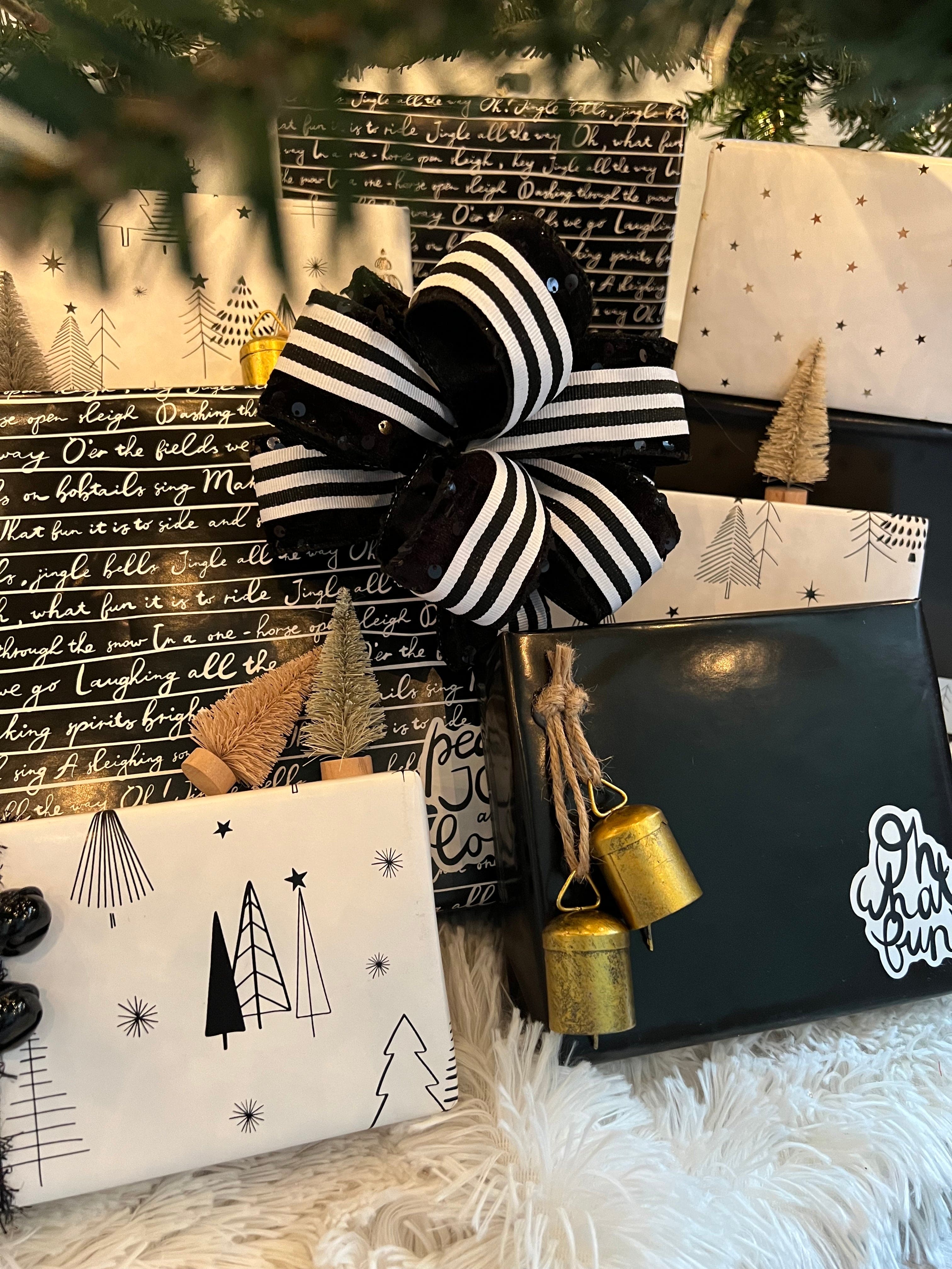Gifts wrapped in black and white paper with a large striped ribbon and small bottle brush trees.
